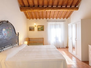 Une chambre avec un plafond en bois, un lit, une table de chevet, une armoire et deux tableaux encadrés accrochés au mur.