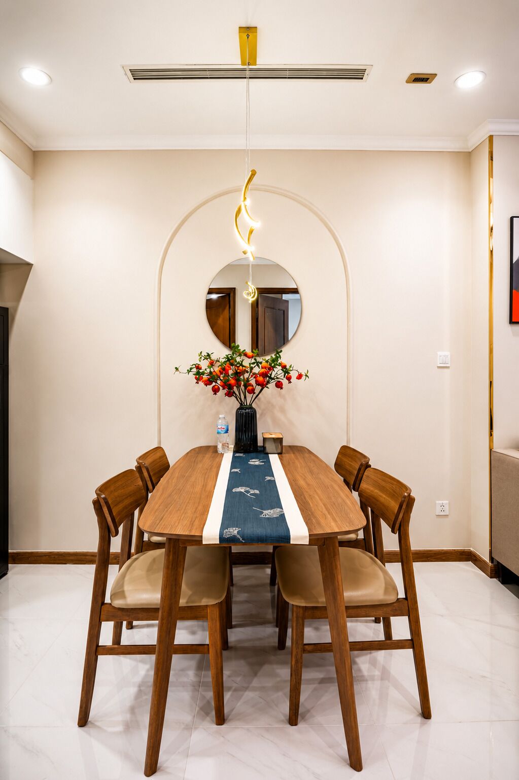 A dining area with a round table, six chairs, a vase with flowers, and a mirror on the wall.