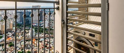 A balcony with a metal railing, a view of a cityscape, and a laundry room with stacked laundry baskets.