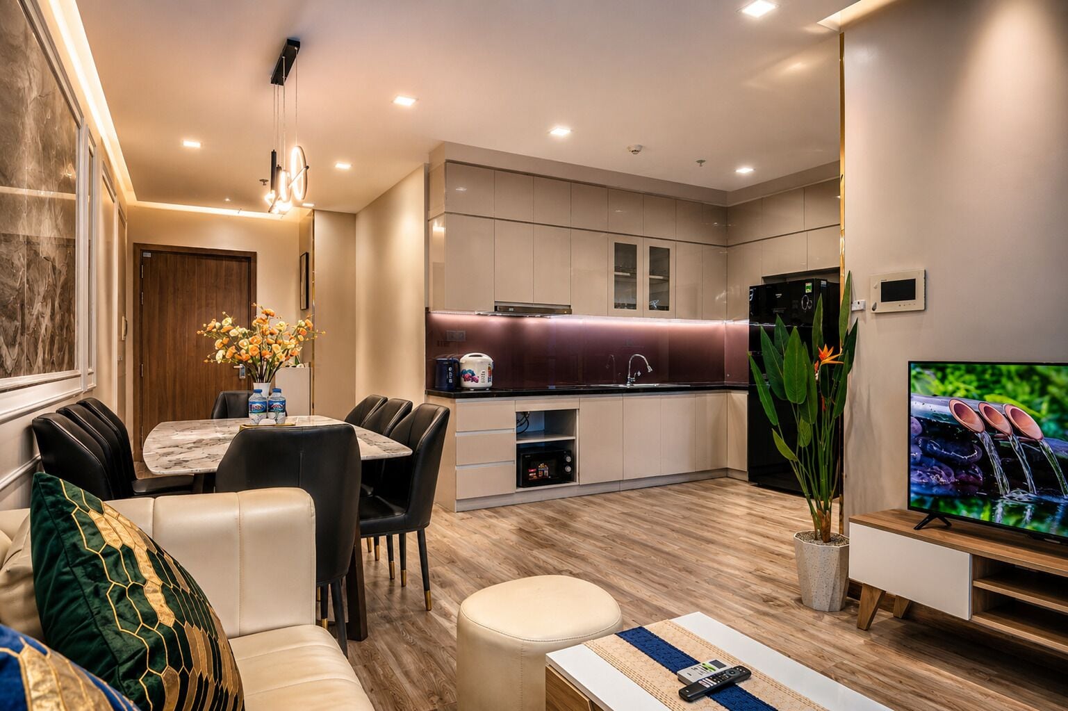 A modern living room with a dining area, kitchen, and a flat-screen TV.