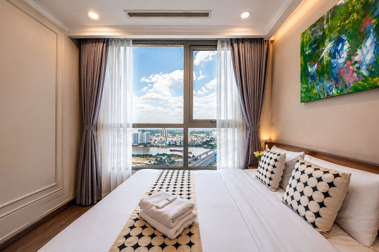 Une chambre d’hôtel avec un grand lit, une vue sur la ville et un tableau accroché au mur.