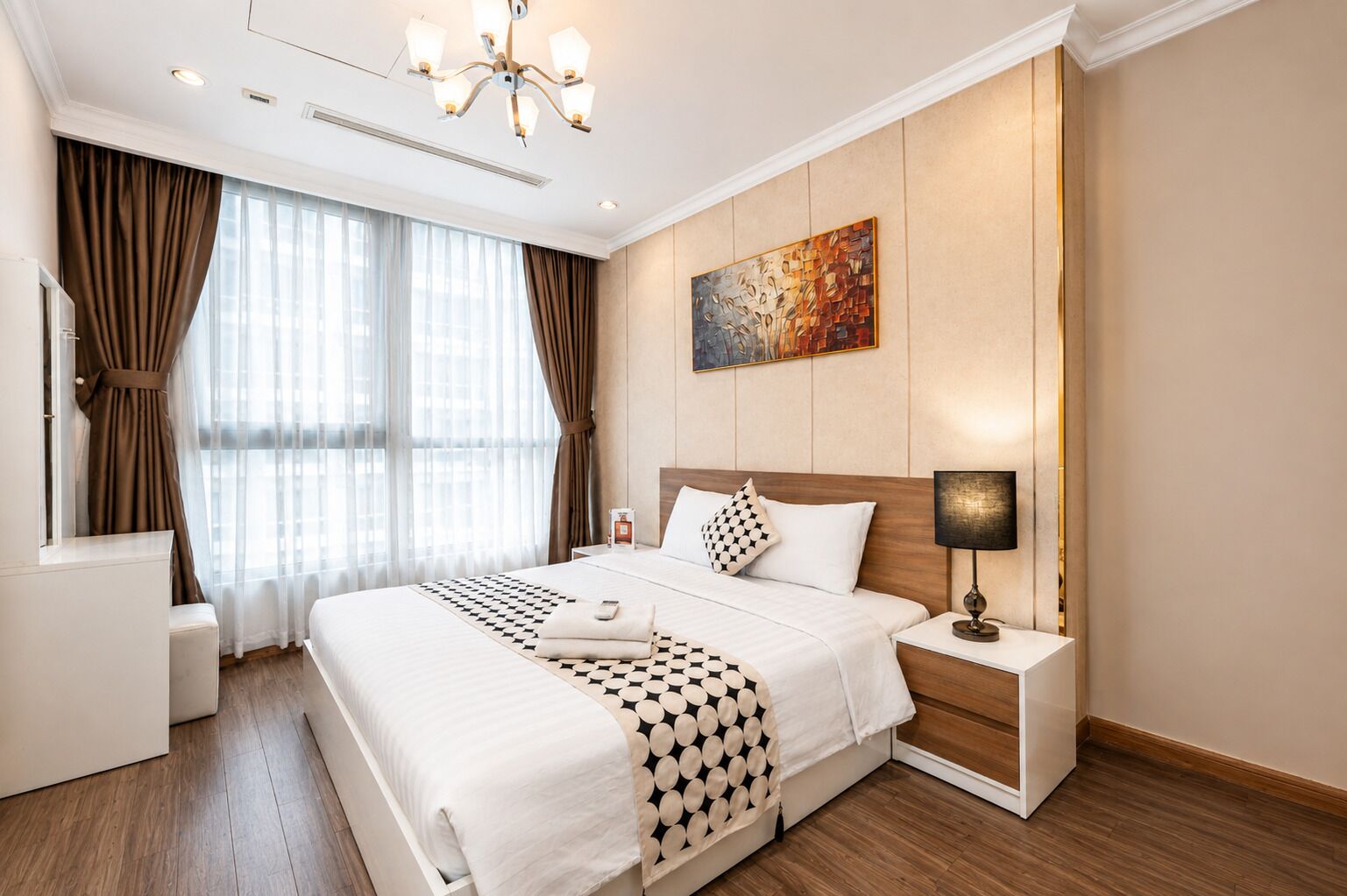 A hotel room with a large bed, a bedside table with a lamp, a painting on the wall, and a window with curtains.