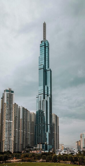 A high-rise building with a glass facade, surrounded by other buildings and a park with palm trees. - Bizport Serviced Apartment HousingHCMC (Ho Chi Minh City)