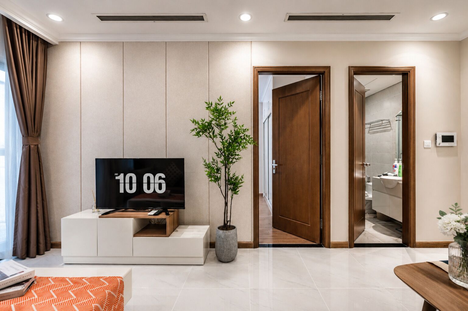 Een moderne woonkamer met een flatscreen televisie, een potplant en een houten deur die naar een badkamer leidt.