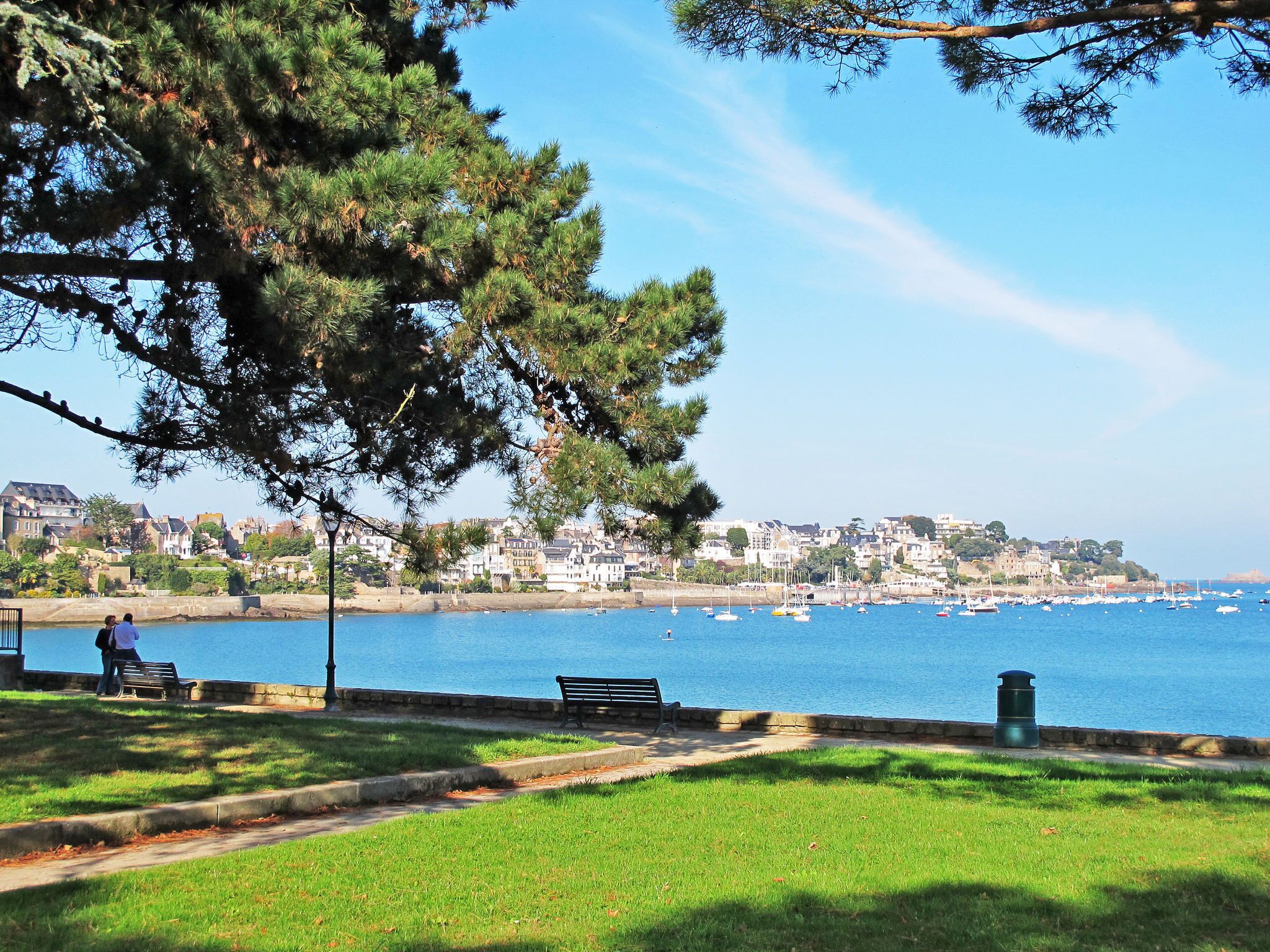 Un parc côtier doté de bancs, d’un sentier et offrant une vue sur une ville située de l’autre côté de l’eau.