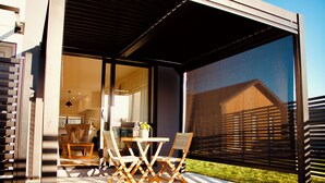 An outdoor patio with a table and chairs, a sliding glass door leading to an interior space, and a view of a house through the door. - Modern 3-Bedroom Family Home Near Racecourse & Brewtown (Upper Hutt)