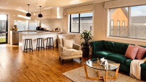 A modern kitchen with a central island, bar stools, a patterned armchair, a green sofa, and a glass coffee table. - Modern 3-Bedroom Family Home Near Racecourse & Brewtown (Upper Hutt)