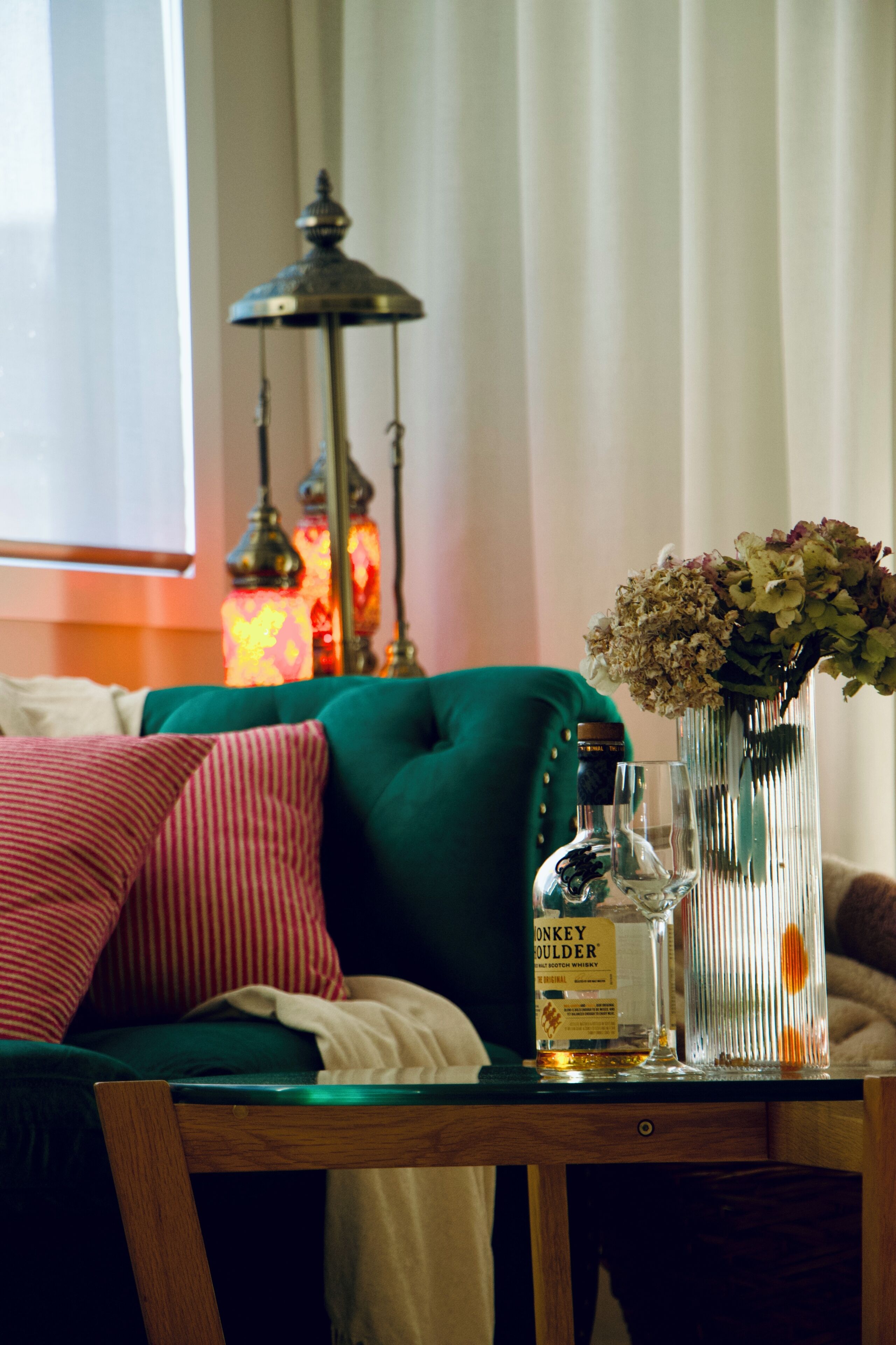 A room with a green sofa, a table with a bottle, a glass, and a vase with flowers.