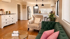 A living room with a green sofa, patterned armchair, and a glass coffee table. - Modern 3-Bedroom Family Home Near Racecourse & Brewtown (Upper Hutt)