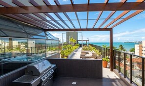 Une terrasse sur le toit équipée d’un barbecue, de chaises longues et de plantes en pot.