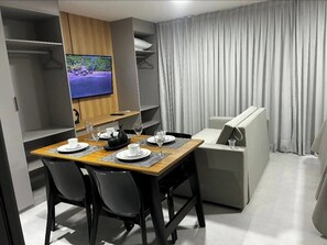 A modern hotel room with a dining area, a flat-screen TV, and a sofa. - Flat Sol & Praia Jardins Al Mare (João Pessoa)