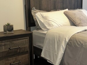 Ein Bett mit weißer Bettwäsche, einem dunklen Kopfteil und einem Nachttisch mit Schubladen.