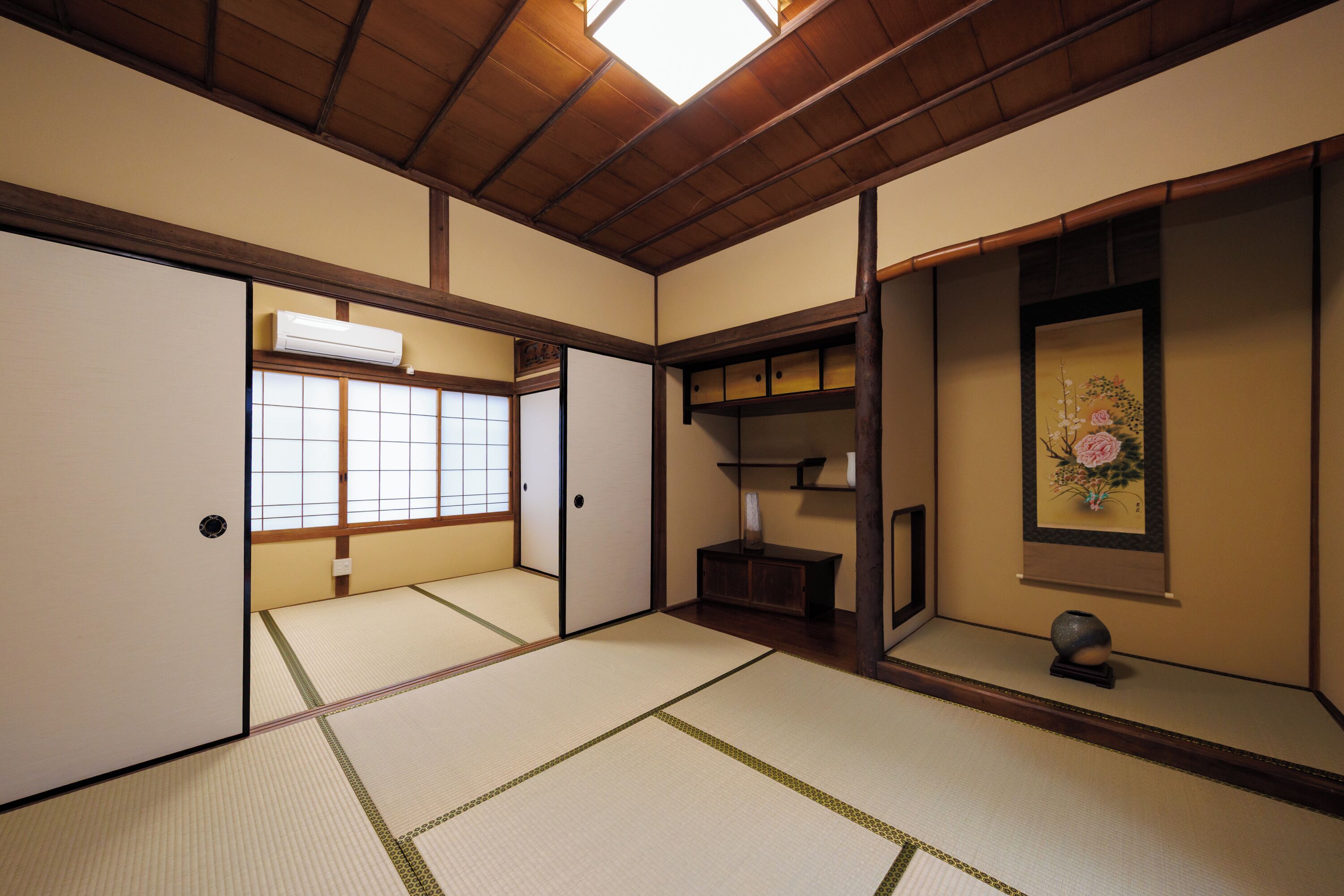 Una habitación japonesa tradicional con suelo de tatami, puertas correderas, techo de madera y aire acondicionado de pared.