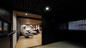 Una habitación con piso de madera, estera de tatami, un sofá, una cama y una ventana con persianas.