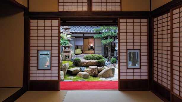 Un interior japonés tradicional con suelo de tatami, puertas correderas y vistas a un jardín.