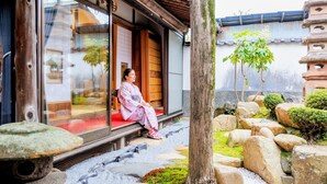 Un edificio japonés tradicional con fachada de madera, un camino de piedra y una persona sentada en un banco afuera.