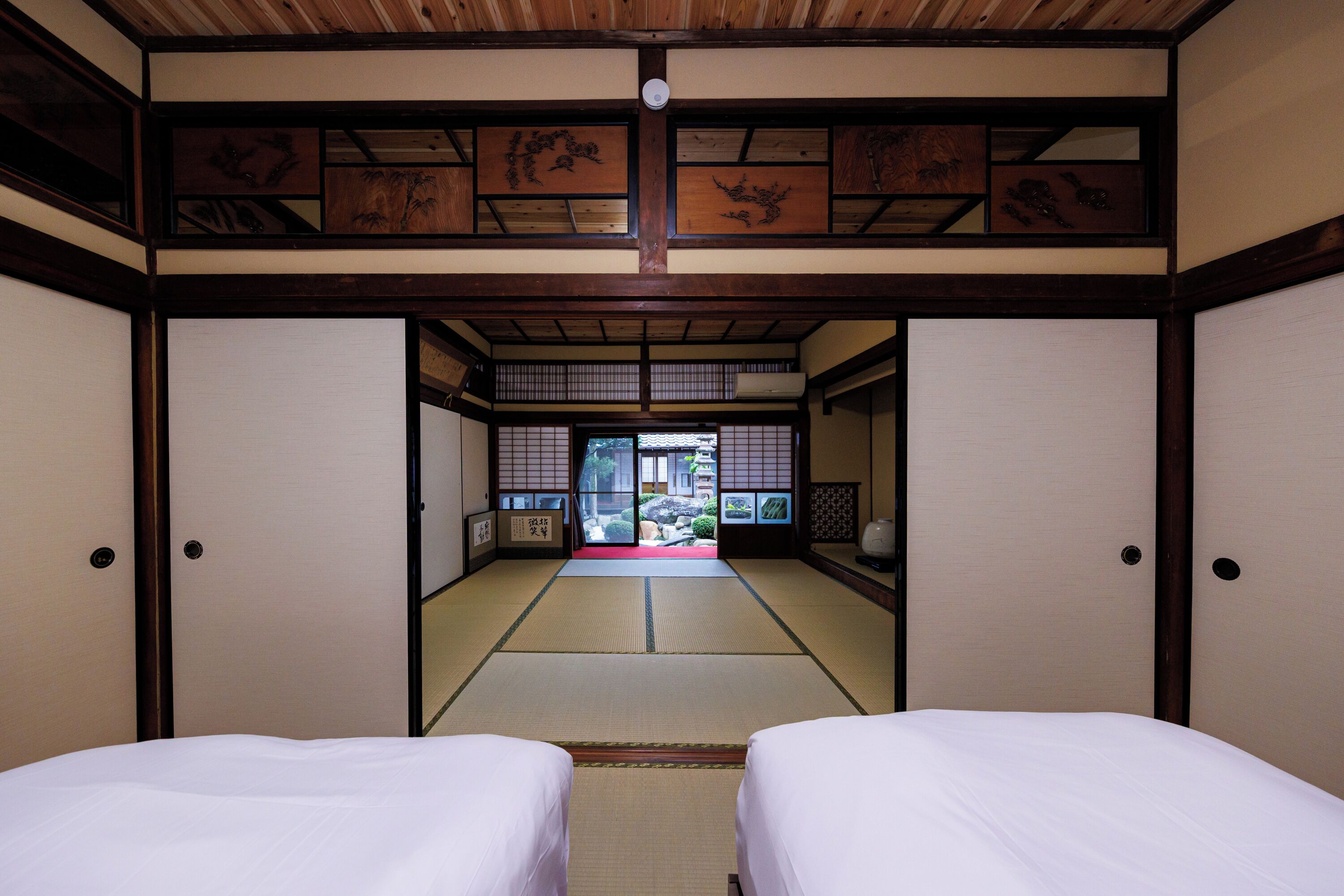 A traditional Japanese room with tatami flooring, shoji screens, and a view of a garden.