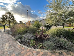 A paved walkway with a garden area featuring various plants and a lamp post.