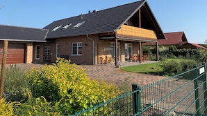 A brick house with a sloped roof, a covered patio, and a fenced garden area. - Vacation apartment on the Arendsee with balcony (near the lake, very quiet location (Arendsee (Altmark))