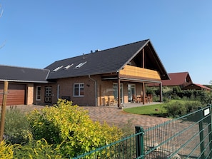 A brick house with a sloped roof, a covered patio, and a fenced garden area.