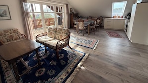 A spacious living area with a dining table, sofa, and chairs, a kitchen with a refrigerator, and a large window. - Vacation apartment on the Arendsee with balcony (near the lake, very quiet location (Arendsee (Altmark))