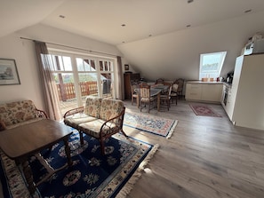 A spacious living area with a dining table, sofa, and chairs, a kitchen with a refrigerator, and a large window.