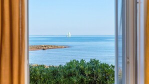 A view through a window of a coastal scene with a sailboat on the water and rocky shoreline. - Villa Numia A: A bright and sunny two-story independent house located right on the beach, with Free WI-FI. (Ostuni)