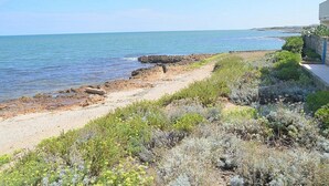 A coastal landscape with a sandy beach, rocky outcrops, and dense shrubbery. - Villa Numia A: A bright and sunny two-story independent house located right on the beach, with Free WI-FI. (Ostuni)