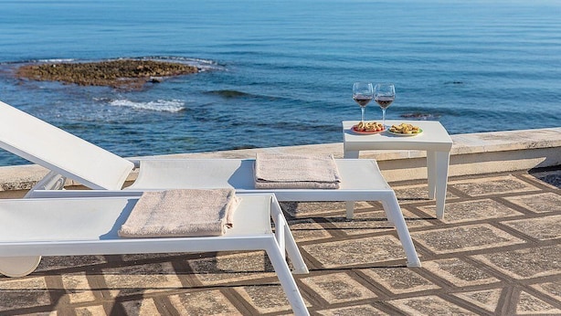 A seaside terrace with white lounge chairs and a table with two glasses of red wine and a plate of food. - Villa Numia A: A bright and sunny two-story independent house located right on the beach, with Free WI-FI. (Ostuni)