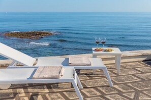 A seaside terrace with white lounge chairs and a table with two glasses of red wine and a plate of food. - Villa Numia A: A bright and sunny two-story independent house located right on the beach, with Free WI-FI. (Ostuni)