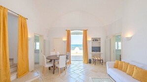 Ein Zimmer mit Esstisch, Stühlen, einer Couch, einem Fernseher und Meerblick.