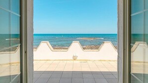 Blick durch eine Glastür auf einen Balkon mit Meerblick und blauem Himmel.