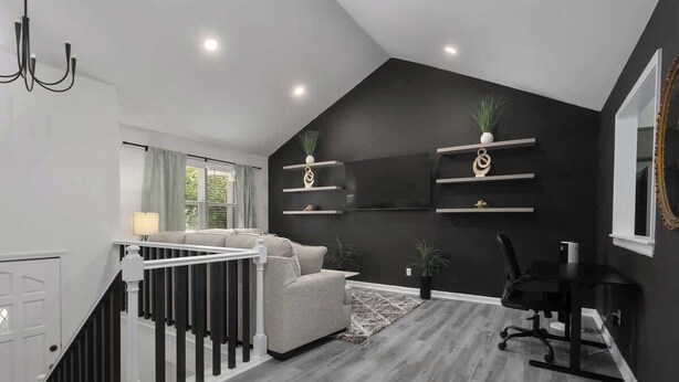 A modern living room with a staircase, a sofa, a desk, and shelves with decorative items. - South KC upscale Corporate Rental (Grandview)