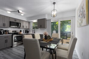 Une cuisine moderne équipée d’appareils électroménagers en acier inoxydable, un coin repas avec une table en verre et une vue sur le jardin arrière.