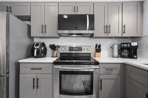 Une cuisine avec des meubles gris, un réfrigérateur en acier inoxydable, un micro-ondes noir, une cuisinière et une machine à café.