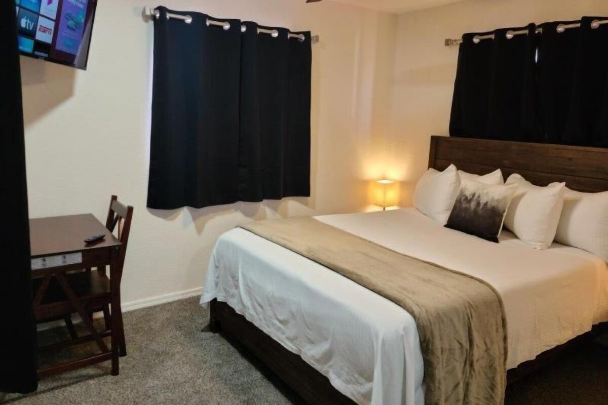 A hotel room with a bed, a desk, a chair, a television mounted on the wall, and a ceiling fan.