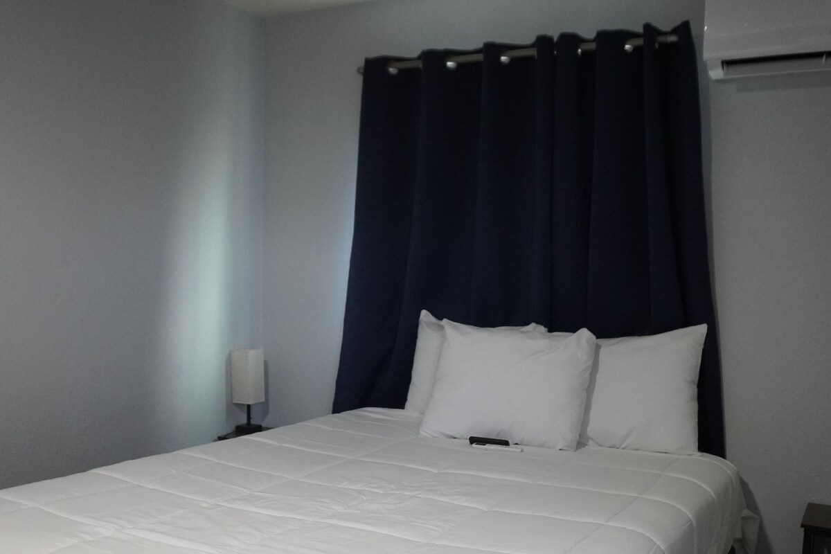 A standard hotel room with a single bed, a nightstand, a lamp, and an air conditioning unit.