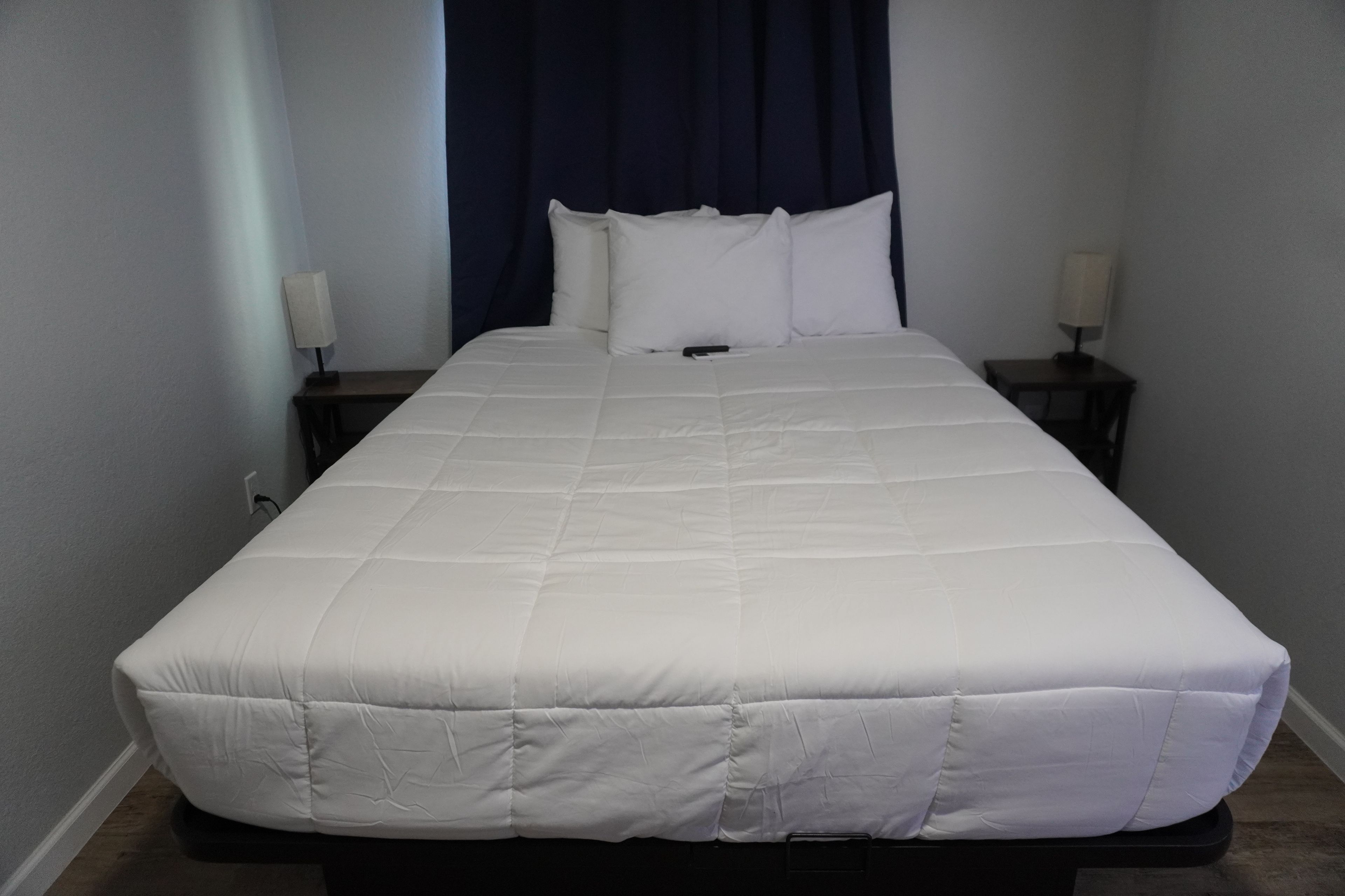 A standard hotel room with a single bed, a nightstand, a lamp, and a dark curtain.