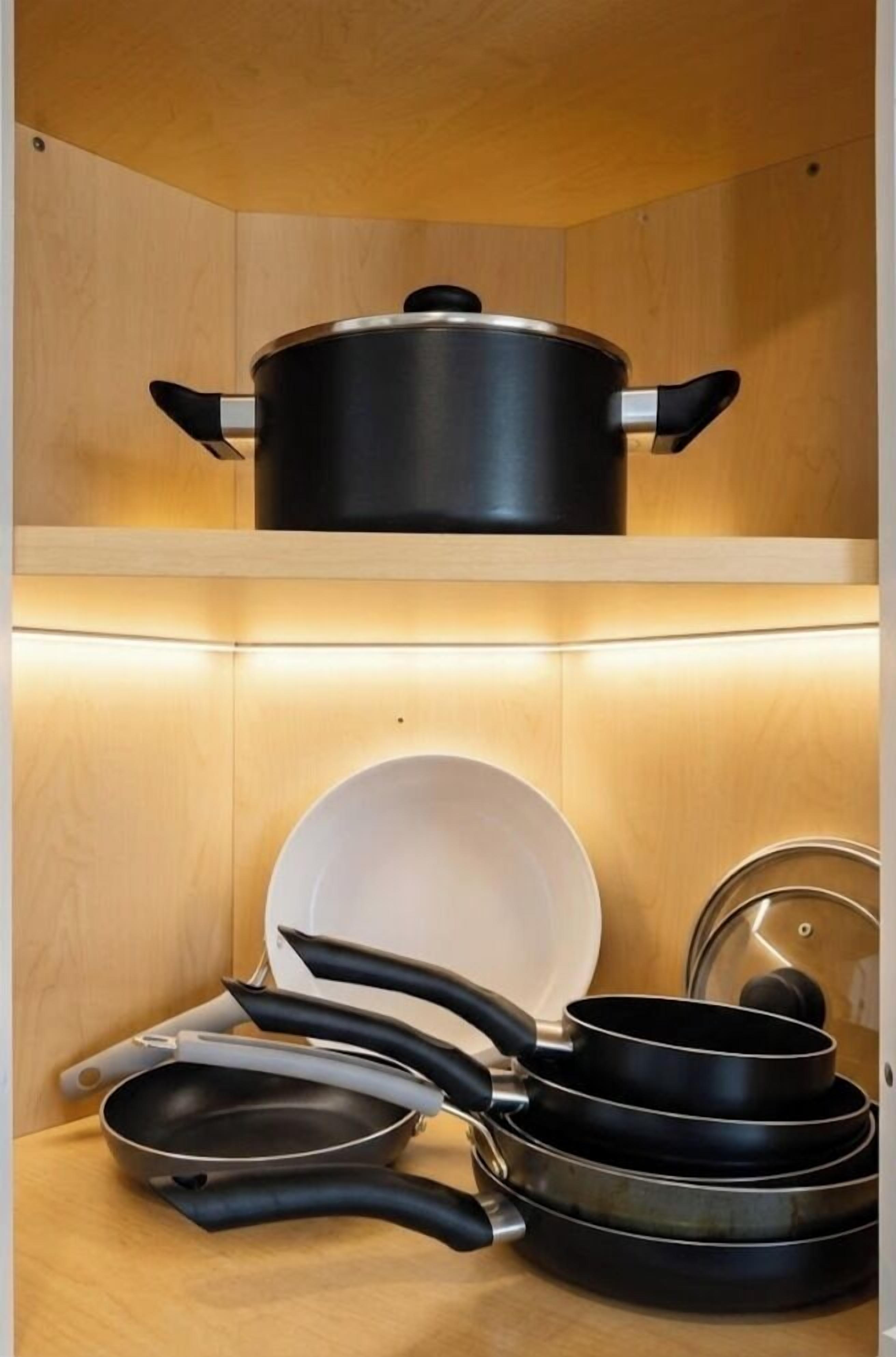Uma cozinha com armários de madeira, uma panela na prateleira superior e diversas panelas na prateleira inferior.