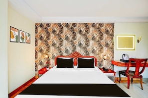 Hotelkamer met een behang, een bed met zwarte kussens, een bureau met stoel en een nachtkastje met lamp.