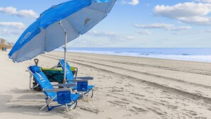 Une plage avec un parasol bleu, deux chaises de plage et une planche de surf.