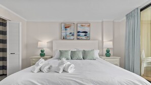 Un lit bien fait, avec du linge de lit blanc et des serviettes pliées, deux lampes de chevet et une œuvre d’art abstraite accrochée au mur.