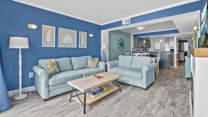 Un salon avec deux canapés bleu clair, une table basse en bois et, au fond, une cuisine.