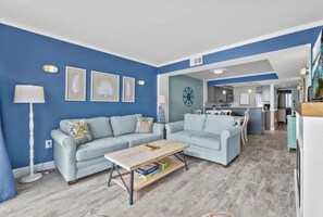 Ein Wohnzimmer mit zwei hellblauen Sofas, einem Holztisch und einer Küche im Hintergrund.