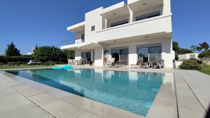Ett modernt hus i två våningar med en swimmingpool, utomhusmöbler och en klarblå himmel.
