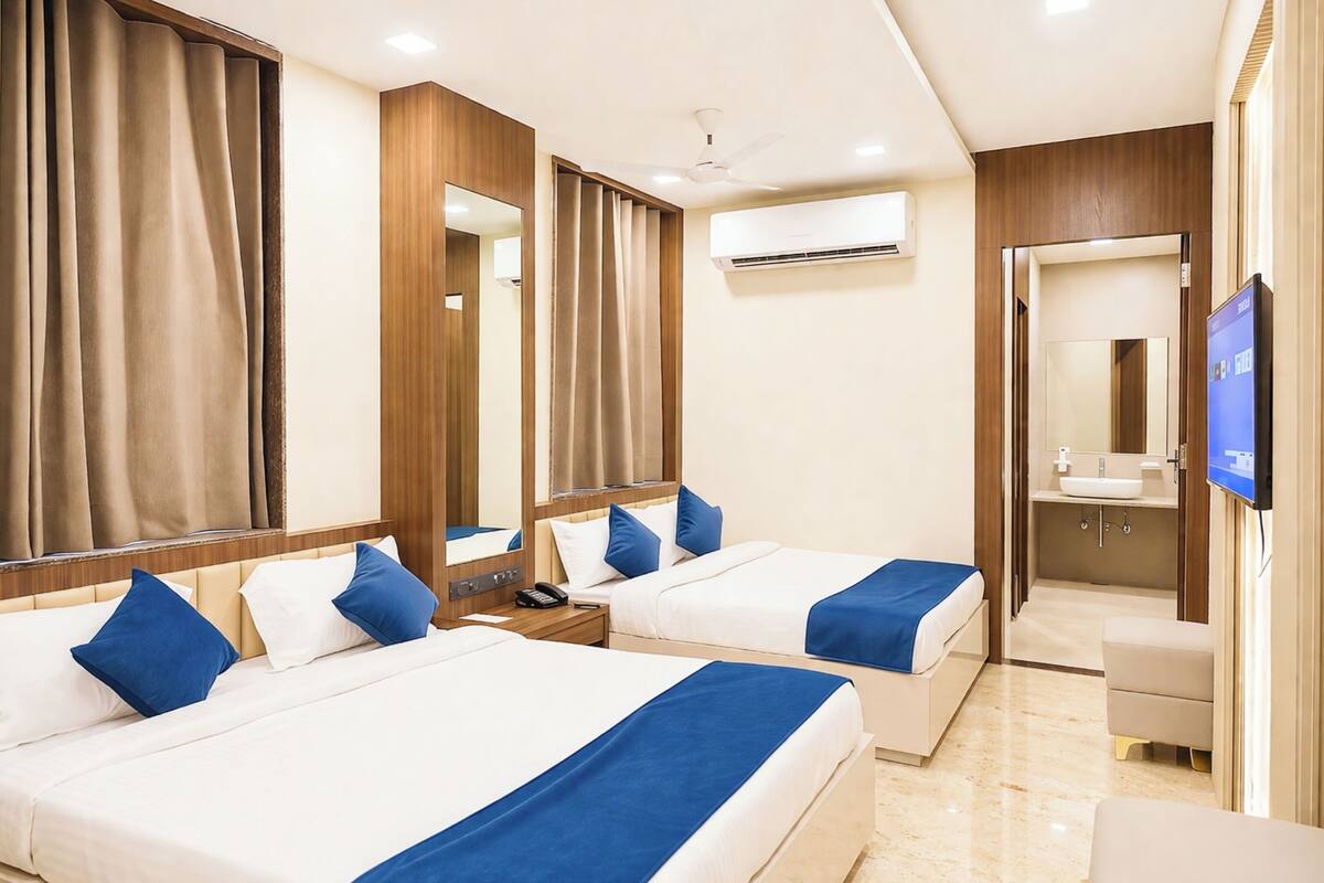 Habitación de hotel con dos camas, televisión, aire acondicionado y baño con lavamanos y espejo.