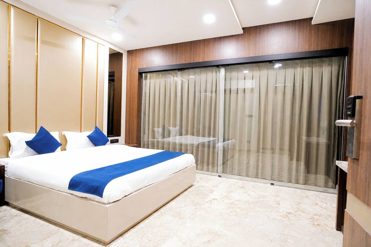 Una habitación de hotel moderna con una cama grande, un muro divisorio de vidrio y una mesita pequeña.