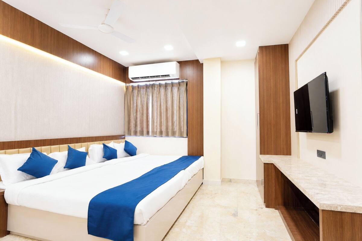 Una habitación de hotel con cama, televisión, ventilador de techo y aire acondicionado.