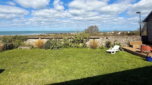 A grassy yard with a white chair, a wooden deck, and a stone wall.