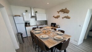 A modern kitchen with white cabinets, a stainless steel range hood, and a dining area set for four with a wooden table and chairs.